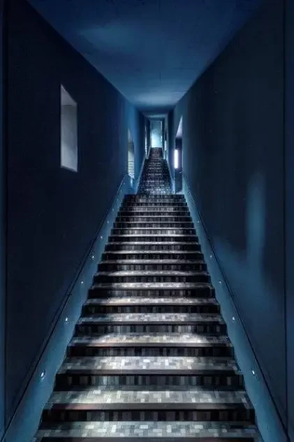 Blau gestrichenes Treppenhaus mit Treppe, die sich nach oben hin stark verj&uuml;ngt