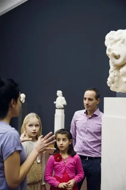 Zwei Kinder mit Vater in der Skulpturenausstellung h&ouml;ren Frau im Vordergrund zu 