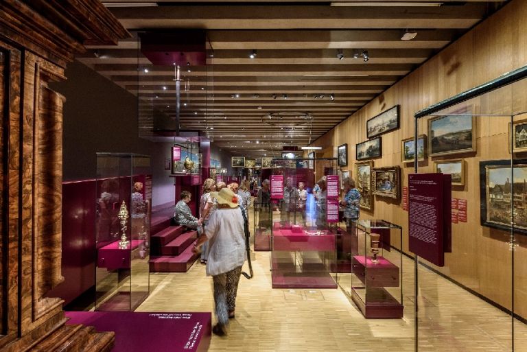 Ausstellung mit Vitrinen und Gem&auml;lden sowie Besucher:innen