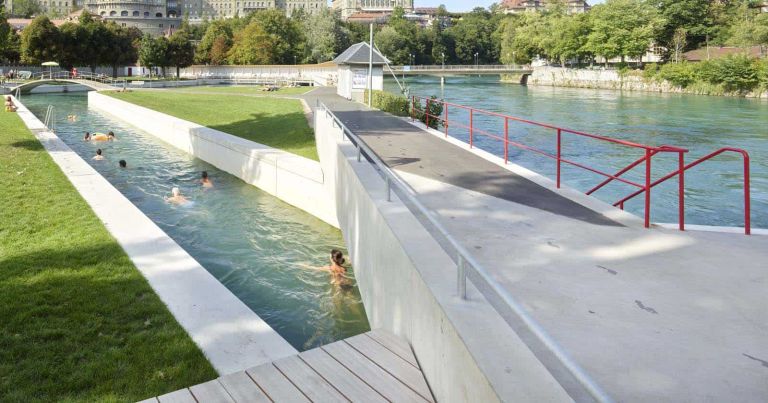 Mehrere Menschen schwimmen in einem Kanal neben einem Fluss in einer Stadt